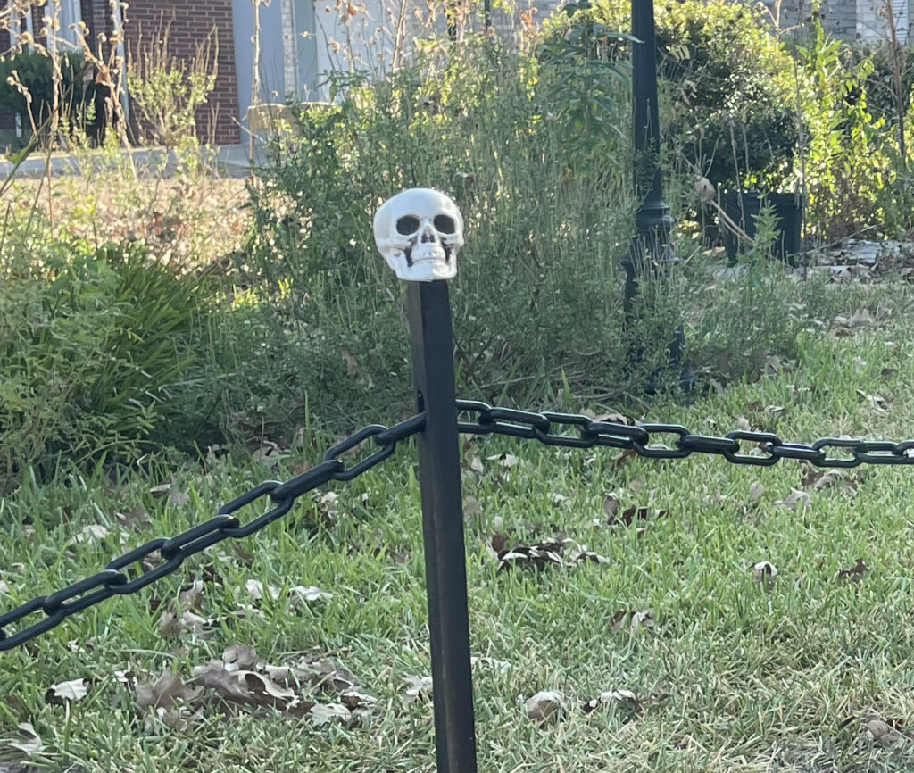 Closeup of a little skull on a black post, with a black chain running through a hole in the post